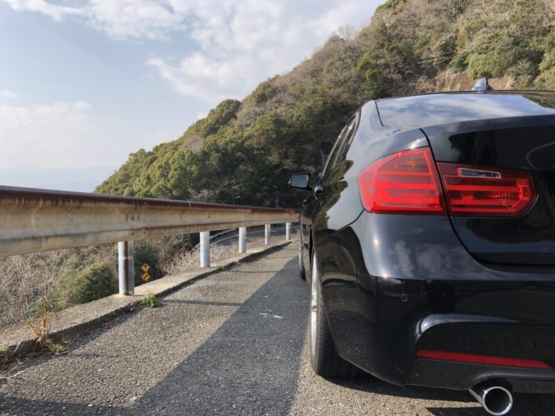 山道に停車した黒いBMW F30 320i Mスポーツの右後方。リアバンパーやランプ、ボディ状態を確認できる